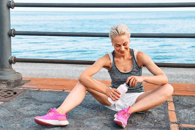 Fit woman relaxes and drinking water on seaside promenade after running and training.