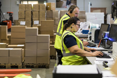 Side view of confident workers using computers at desk in distribution warehouse