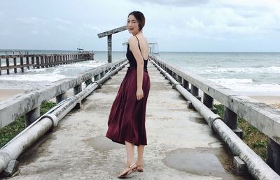 Woman standing on railing by sea against sky