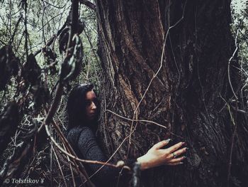 Portrait of young man standing by tree trunk in forest