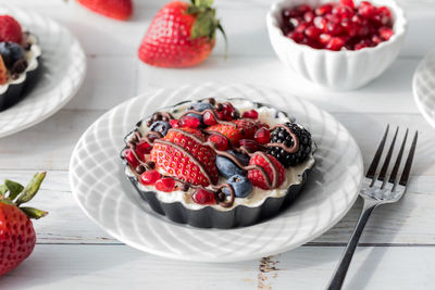 A mixed berry cheesecake tart drizzled with chocolate, on a white wooden table.