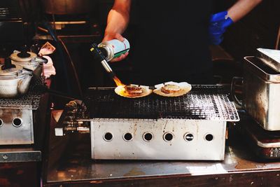 Midsection of chef holding flaming torch while preparing food on barbeque at restaurant