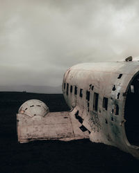 Abandoned airplane at beach against cloudy sky