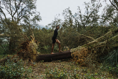 Side view of young man in forest against sky