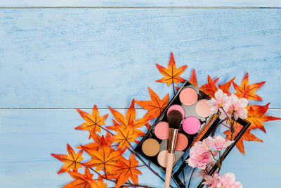 Directly above shot of make-up with autumn maple leaves on table