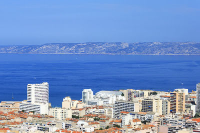 High angle view of townscape by sea against blue sky