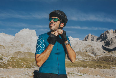 Young man wearing sunglasses standing on mountain against sky