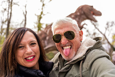 Happy middle aged couple taking a selfie in front a model t-rex in a public park