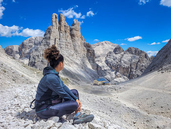 Rear view of man sitting on mountain against sky