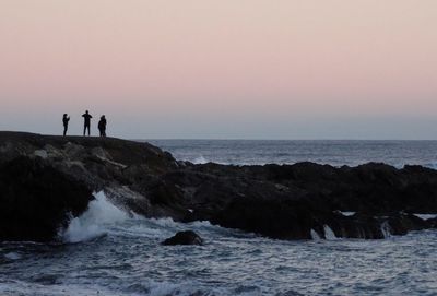Silhouette people standing on beach against sky during sunset