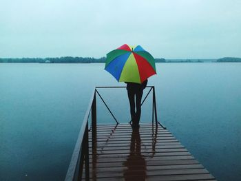 Person with umbrella standing on pier over lake