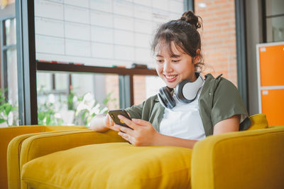 Young woman using phone while sitting on sofa at home