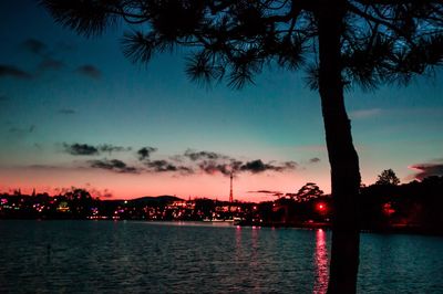 Silhouette trees by lake against sky at sunset