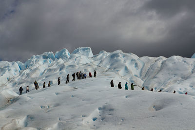 Low angle view of people walking at perito moreno glacier against cloudy sky