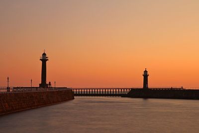 Lighthouse by sea against sky during sunset