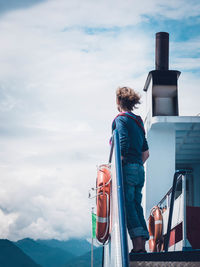 Rear view of man standing by railing against sky