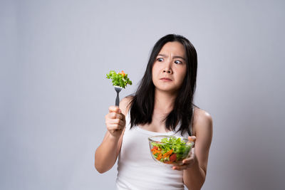 Portrait of young woman holding ice cream against white background