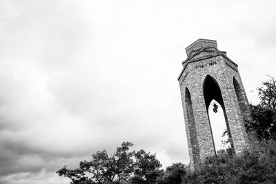 Low angle view of tower and trees against cloudy sky