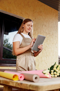 A smiling female florist stands with a tablet in her hands next to a table with bouquets of tulips