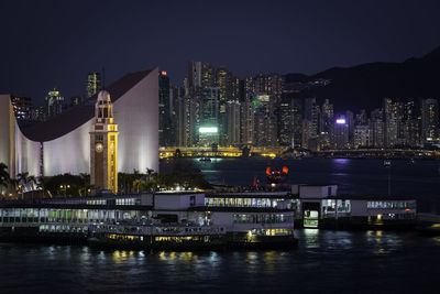 Illuminated buildings by river against sky at night