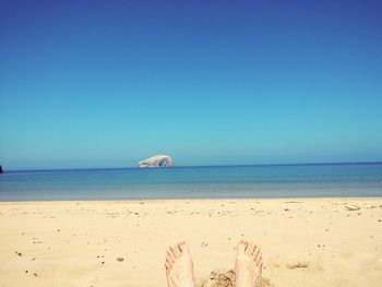 Low section of man at beach against clear blue sky