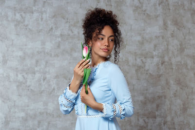 Beautiful woman holding tulip while standing against wall