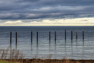 Wooden posts in sea against sky