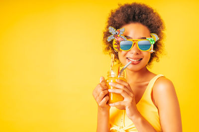Portrait of smiling young woman wearing sunglasses against yellow background