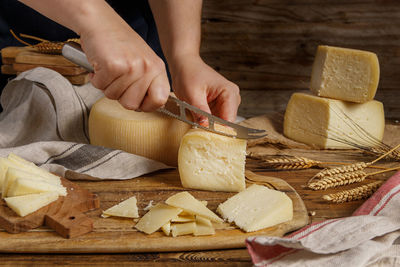 Hands cutting pieces of fresh homemade cheese on a wooden board close up