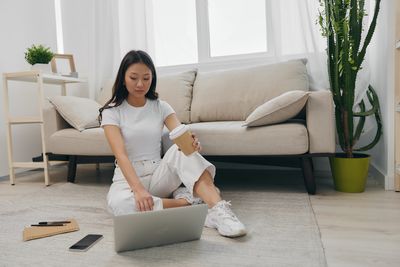 Young woman using laptop while sitting on sofa at home