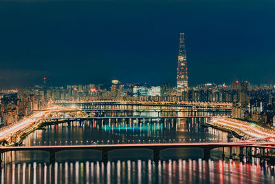 Illuminated bridge over river by buildings in city at night