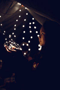 Portrait of young woman holding illuminated light in the dark