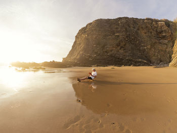 Portugal, senior man sitting at beach, reading book