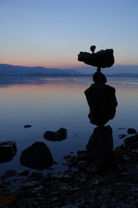 Stone stack on rock at sea shore against sky during sunset