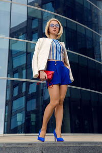 Young business woman in short blue trunks standing and waiting for a meetingfrom the bank of glass