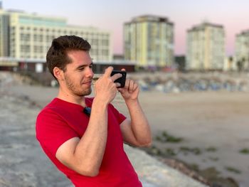 Young man photographing with camera while standing at beach