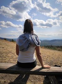 Rear view of woman sitting on land against sky