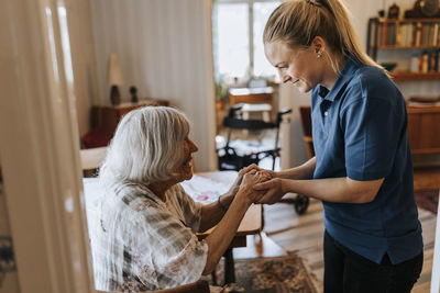 Smiling female healthcare worker holding hands of senior woman at home