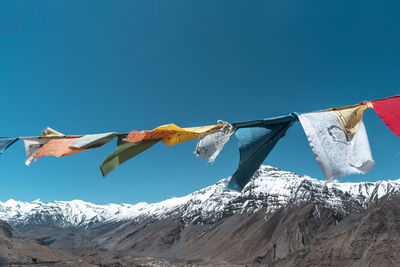 Low angle view of flags against snowcapped mountains against clear blue sky