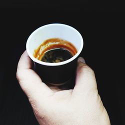 Close-up of hand holding tea cup against black background