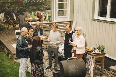 Smiling elderly male and female friends talking while enjoying dinner party at back yard