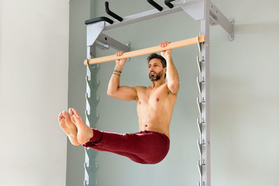 Full length of shirtless young man sitting on wall