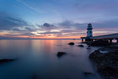 Lighthouse by sea against sky during sunset