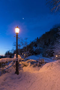 Illuminated street light on snow covered landscape at night