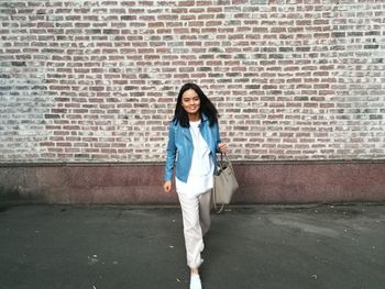Portrait of young woman standing against brick wall