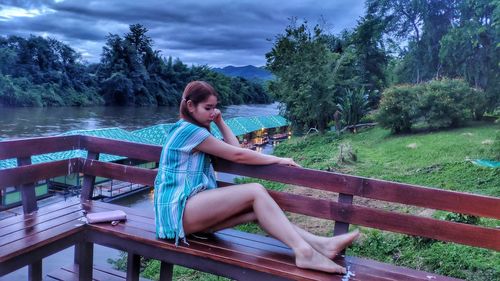 Young woman sitting on bench against trees