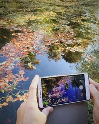 Reflection of person photographing on mobile phone in park