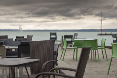 Empty chairs and table by sea against sky