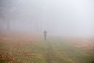 Rear view of man standing on landscape in foggy weather