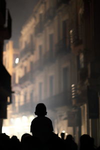 Rear view of silhouette people against illuminated buildings at night